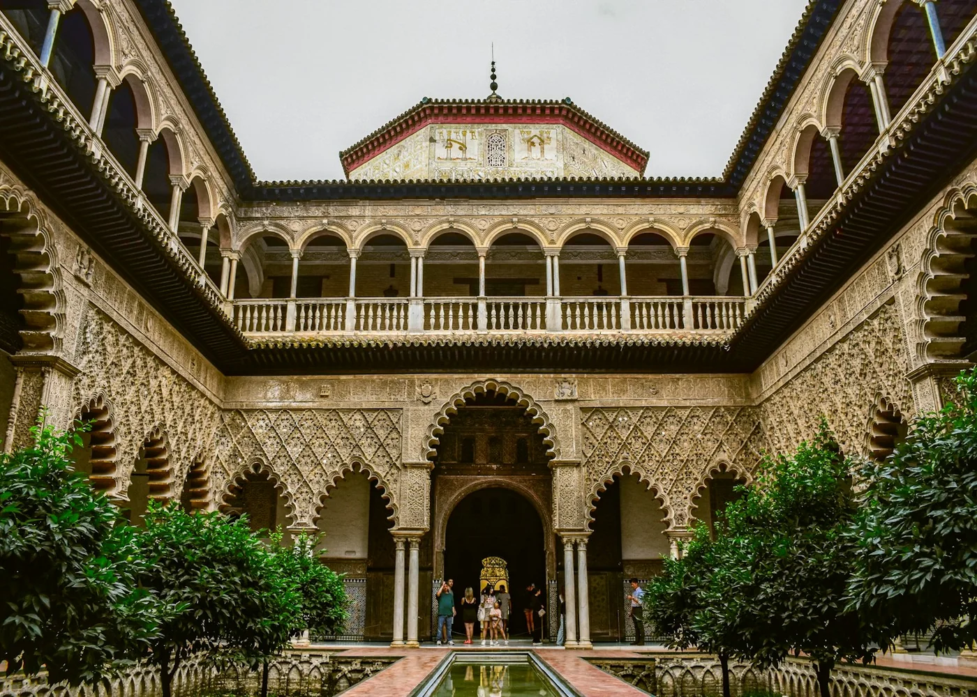 A Mudéjar palace courtyard with a horseshoe-arched doorway, carved plasterwork and orange trees, at the Real Alcázar of Seville (representative photograph of Andalusian palace architecture, not El Palacio Andaluz's own building)