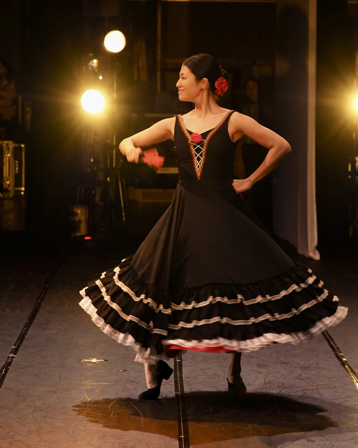 Flamenková tanečnice v černo-bílých volánových šatech, v půlobrátce na osvětleném jevišti s červeným květem ve vlasech (reprezentativní fotografie flamenkového vystoupení, nikoli El Palacio Andaluz)