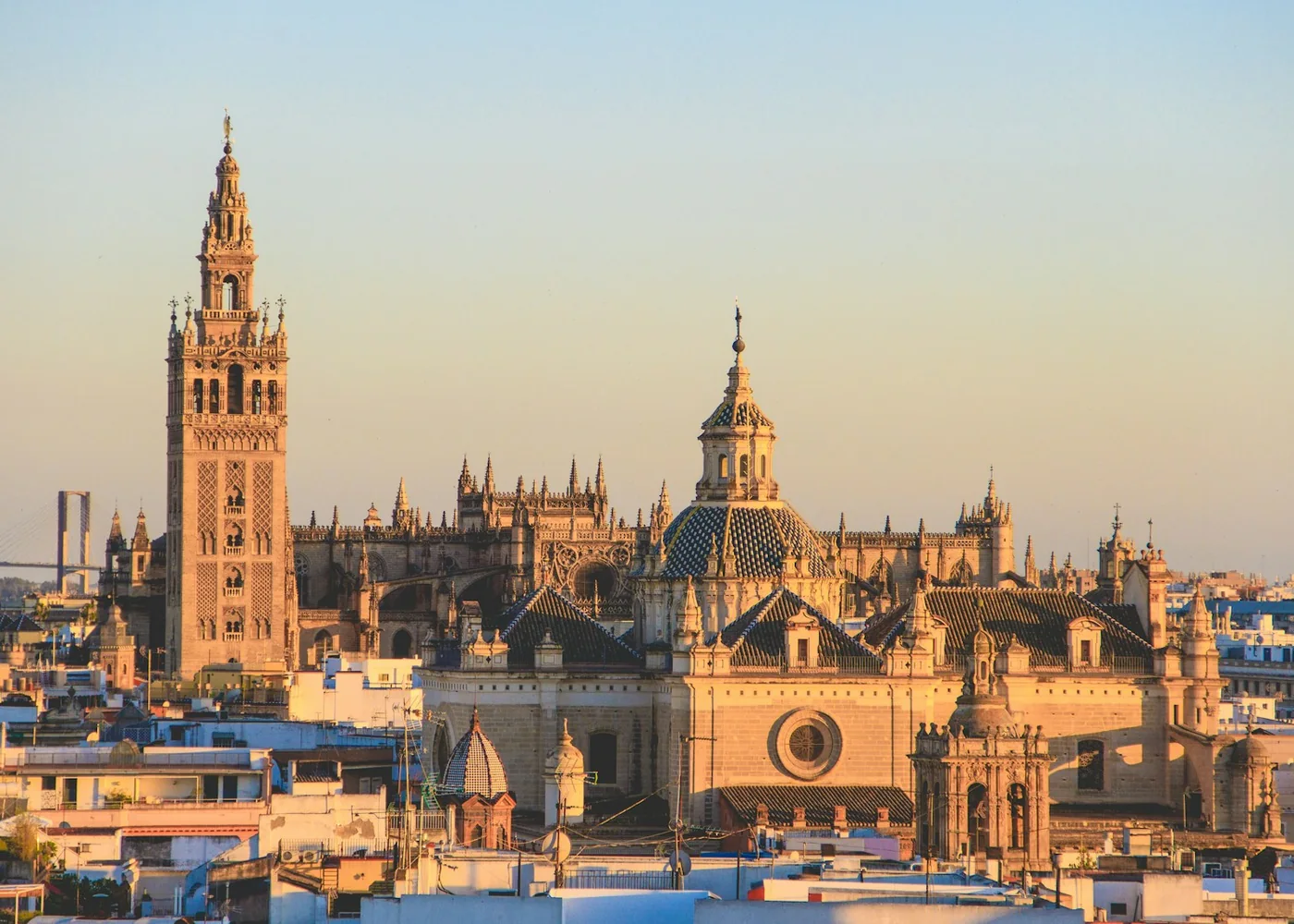 Věž Giralda a sevillská katedrála tyčící se nad střechami sevillského starého města při západu slunce (reprezentativní fotografie historického centra Sevilly, přes řeku od Isla de la Cartuja)