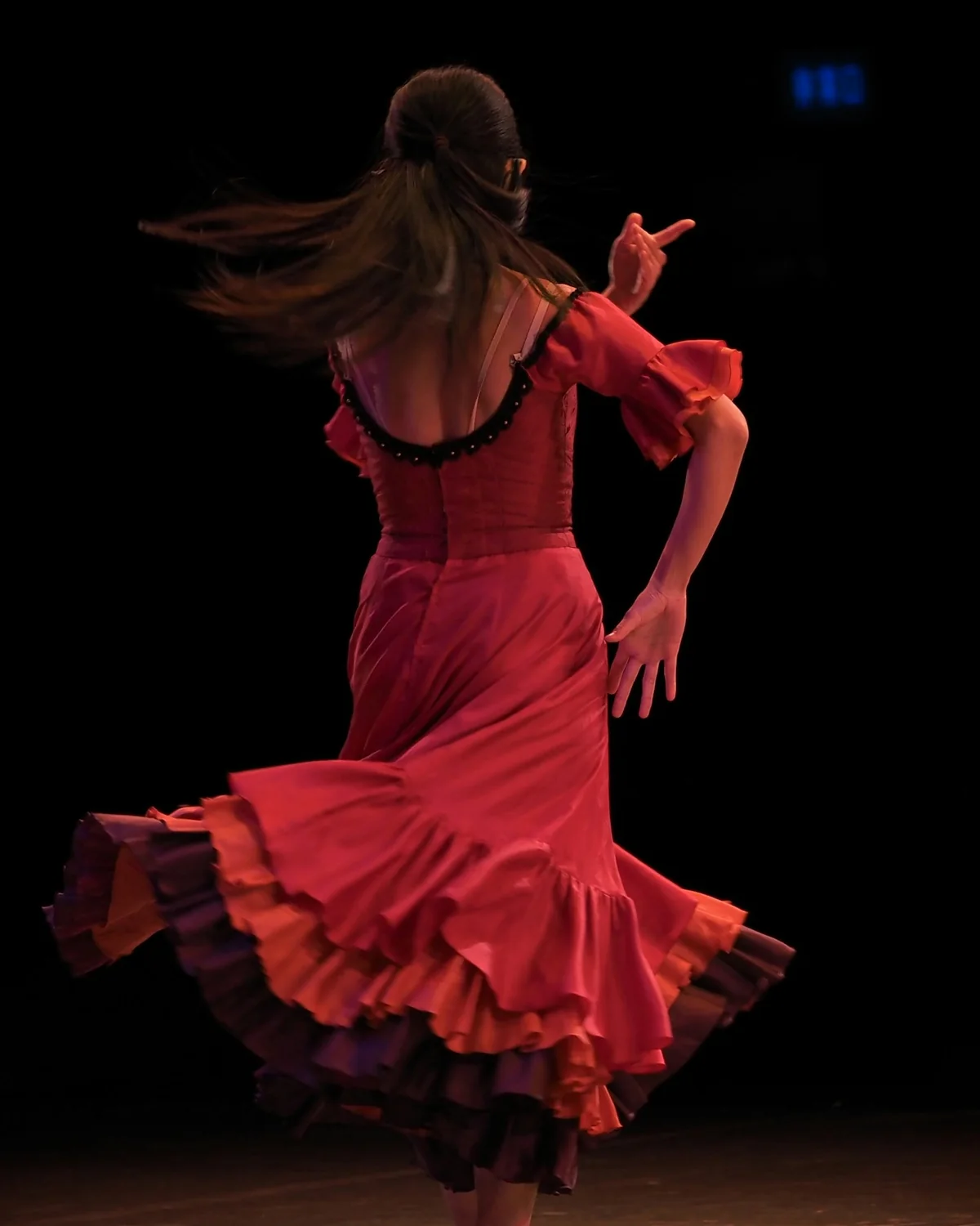 Flamenková tanečnice v červených volánových šatech točící se na tmavém jevišti, vlasy v pohybu (reprezentativní fotografie flamenkového vystoupení, nikoli El Palacio Andaluz)