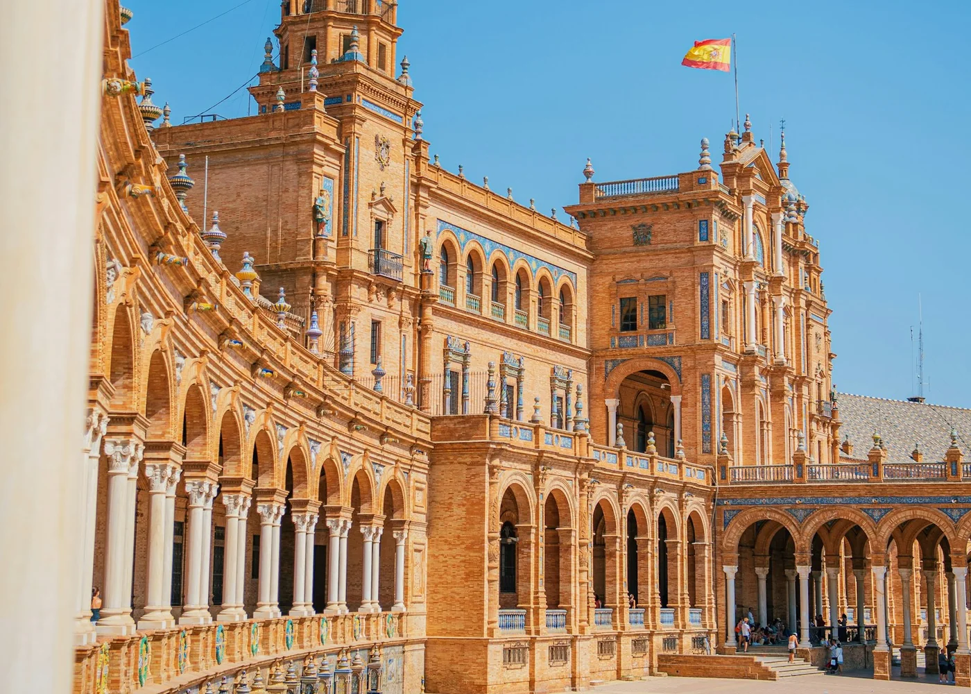 Dlaždicová, zakřivená arkáda a věže Plaza de España v Seville pod modrým nebem (reprezentativní fotografie sevillské azulejo dlažby, nikoli vlastní výzdoba El Palacio Andaluz)